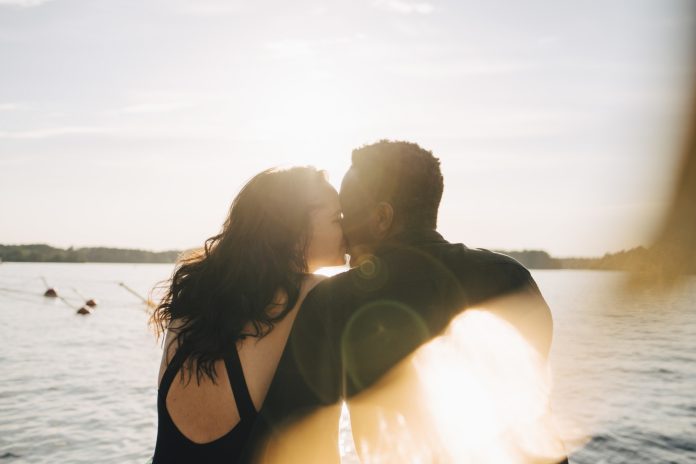 Multi-ethnic couple kissing while sitting against lake during summer Guía para reconocer el amor verdadero según la psicología